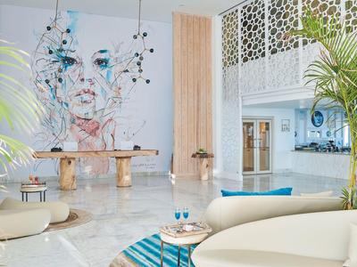 Lichte moderne hotelhal met kunstmuur, ronde banken, palmbomen en marmeren vloer.