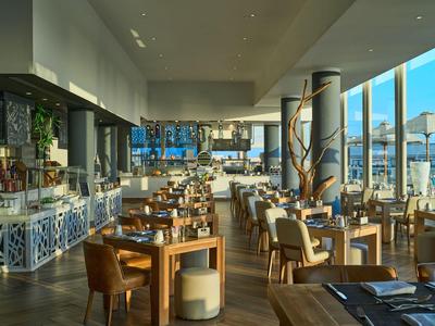 Ristorante luminoso con tavoli in legno e grandi finestre con vista sull'acqua.