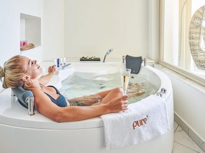 Donna che si rilassa in una vasca da bagno con un bicchiere di vino accanto a una finestra in un'area spa.