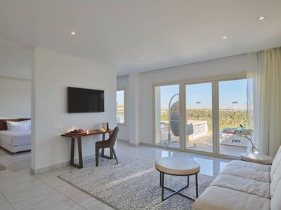 Bright hotel room with living area, terrace, and landscape view.