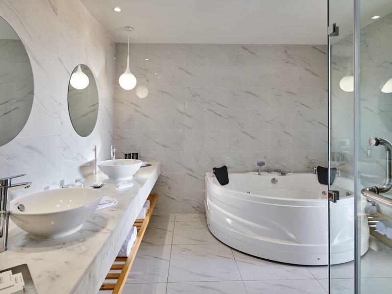 Modern bathroom with round bathtub, two sinks, and marble tiles.