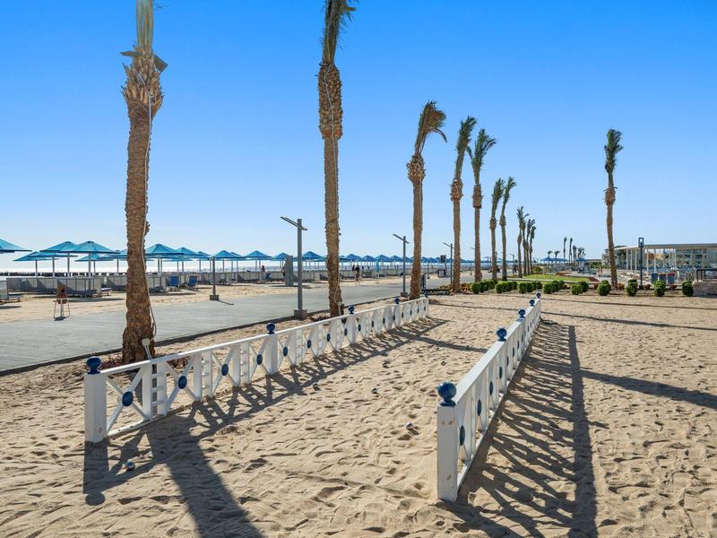 Strand mit Palmen und Stühlen unter Sonnenschirmen bei klarem Himmel
