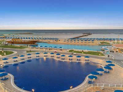 View of a pool with blue umbrellas and the sea in the background on a calm day.