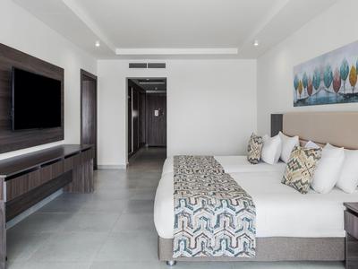 Modernes Hotelzimmer mit großem Doppelbett, TV an der Wand und einem bunten Bild über dem Bett.