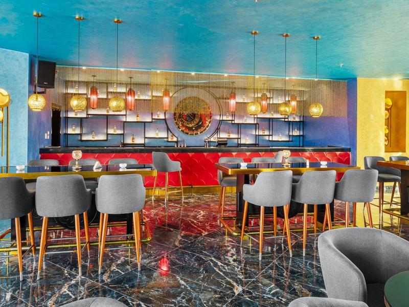 Moderner Hotelbarbereich mit blauem Deckenakzent, roten Stühlen und schwarzem Marmorboden.