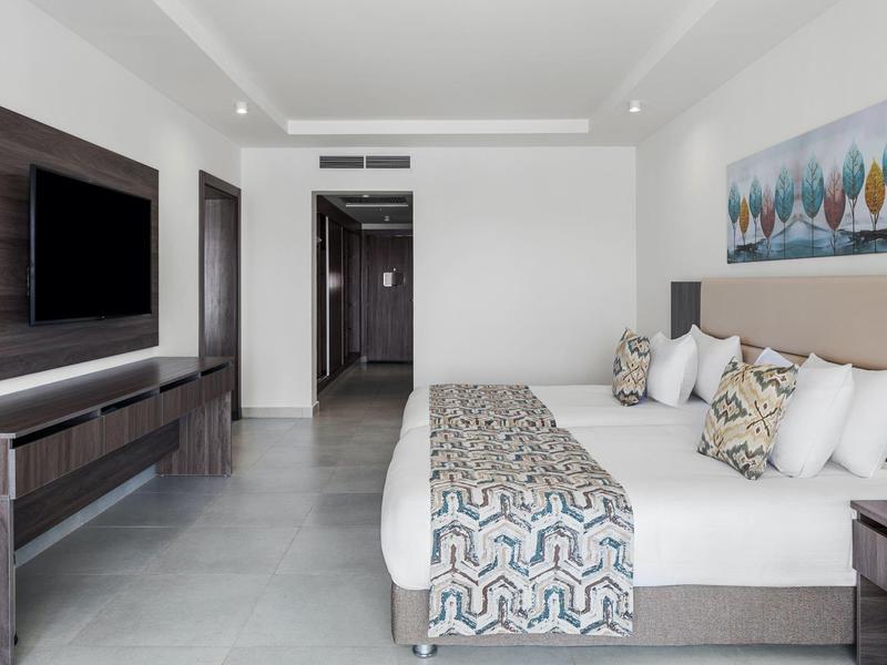 Modernes Hotelzimmer mit großem Doppelbett, TV an der Wand und einem bunten Bild über dem Bett.