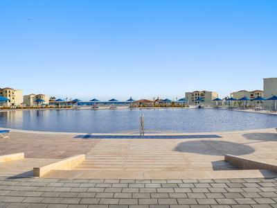 Groot hotelzwembad met ligstoelen en gebouwen onder een heldere blauwe lucht