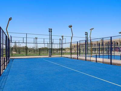 Leeres, blaues Paddle-Tennisfeld mit Umzäunung und klarem Himmel im Hintergrund.