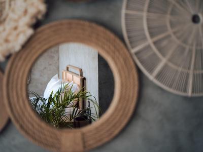 Rotan wandspiegels die planten en een ingelijst kunstwerk reflecteren op een grijze muur.