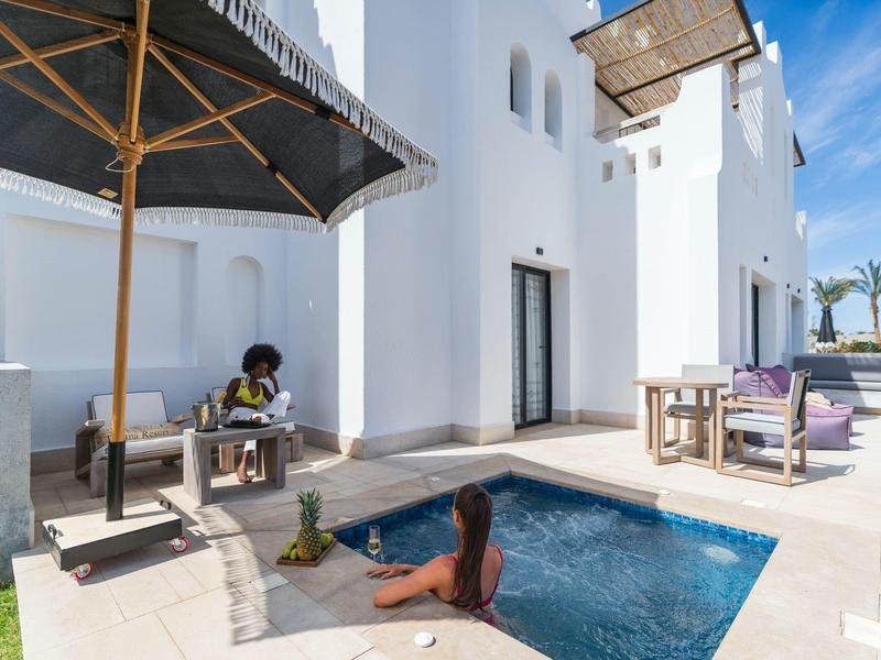 Moderne witte villa met klein zwembad, ligstoelen en persoon die ontspant in het water.