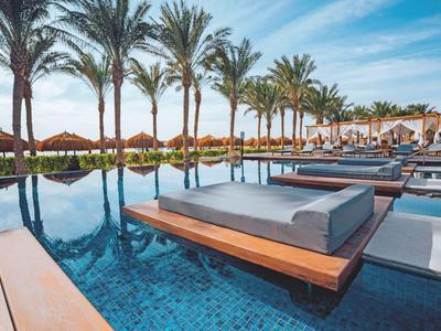 Moderner Poolbereich mit Sitzliegen, Palmen und klarem Himmel in einem Resort.