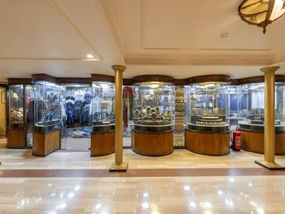 Heldere hotellobby met glanzende vloer, gouden zuilen en vitrines met decoraties.