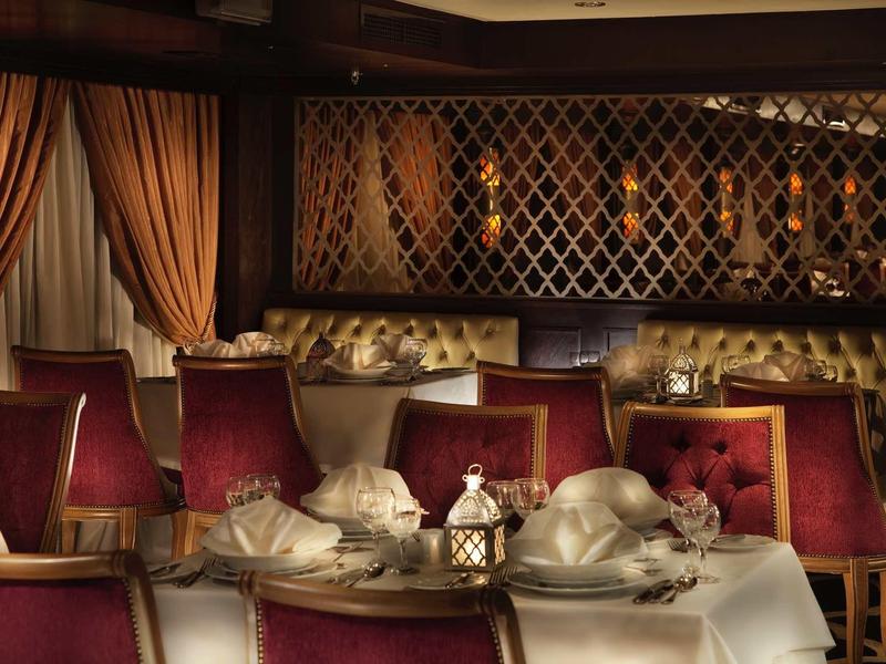 Elegant dining room with red chairs, beige curtains, and neatly arranged tables with white linens.