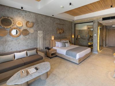 Habitación de hotel moderna con cama, sofá, espejos redondos y detalles de madera.