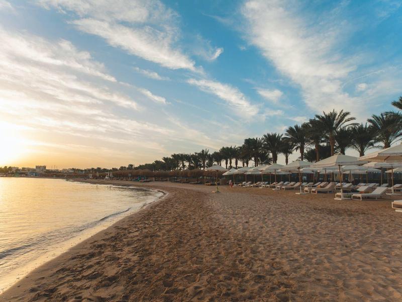 Piaszczysta plaża z parasolami i palmami o zachodzie słońca.