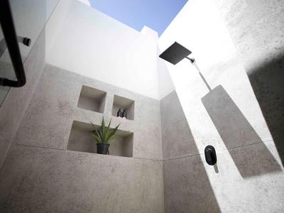 Modern outdoor shower area with built-in shelves and a tall showerhead under blue sky.