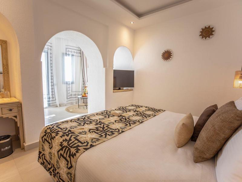 Cozy hotel room with double bed, patterned bed runner, arched doorway, and modern decor.