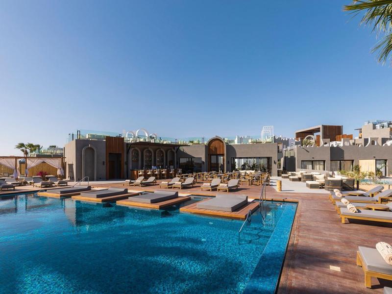 Área moderna de piscina con tumbonas y agua azul bajo el cielo despejado en un hotel.