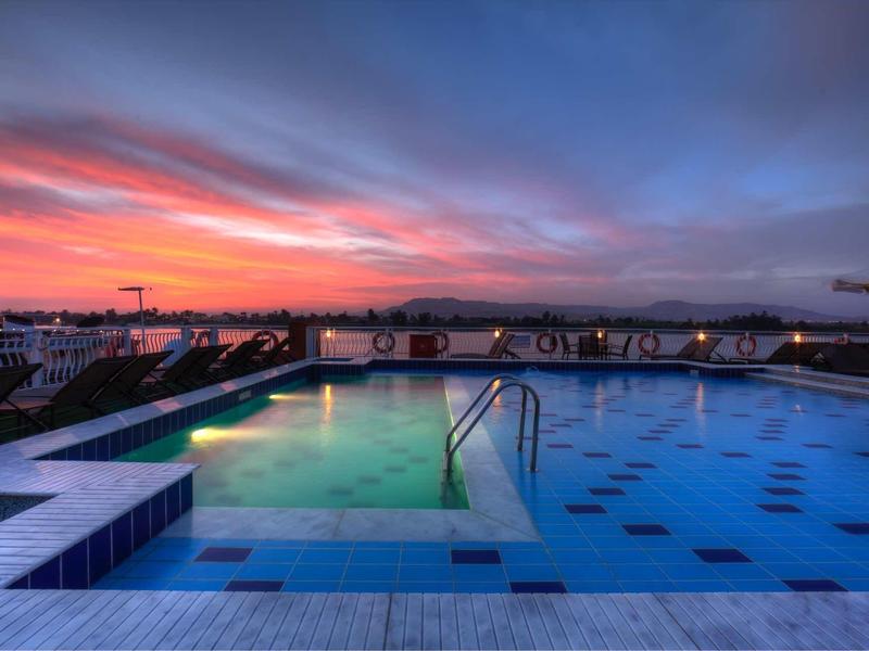 Atardecer en una piscina al aire libre iluminada con vista al mar y la puesta de sol.