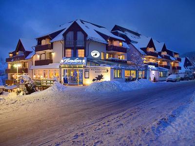 Großes, beleuchtetes Hotel in verschneiter Berglandschaft bei Abenddämmerung mit blauem Himmel.