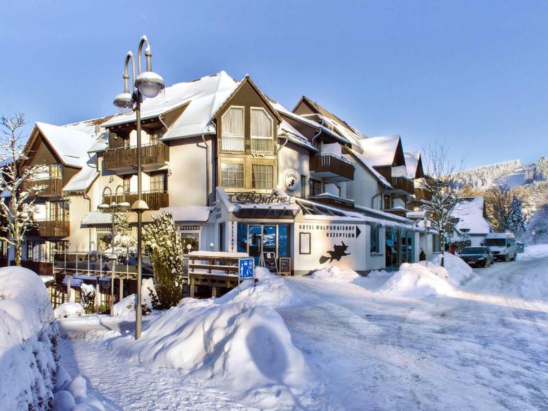 Großes Haus mit spitzen Dächern, umgeben von tiefem, weißem Schnee und blauem Himmel.