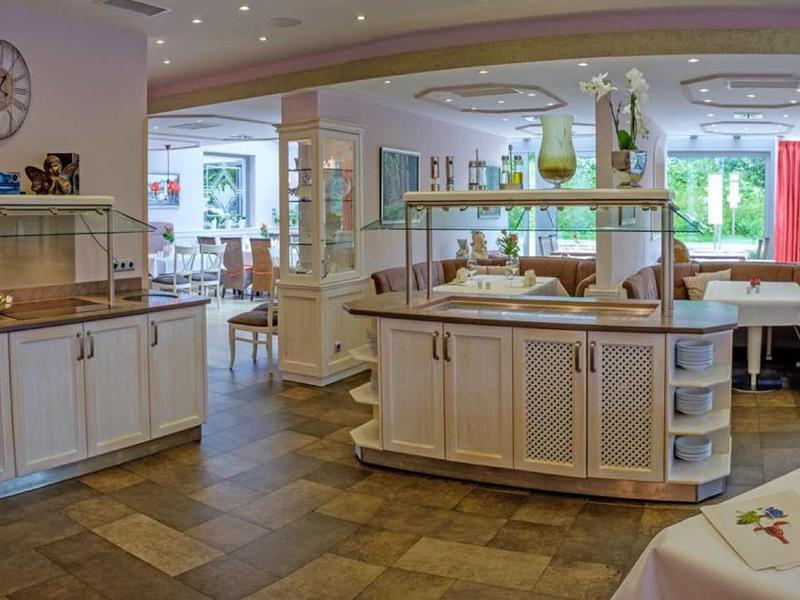 Großes, helles Restaurant mit Holzboden, weißen Möbeln und gedeckten Tischen in angenehmer Atmosphäre.