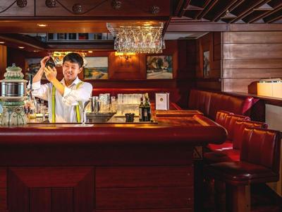 Barkeeper mixt einen Drink in einer gemütlichen Bar mit dunklem Holz und rotem Leder.