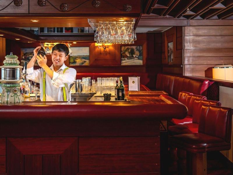 Barman die een drankje maakt in een gezellige houten bar met rode barkrukken.