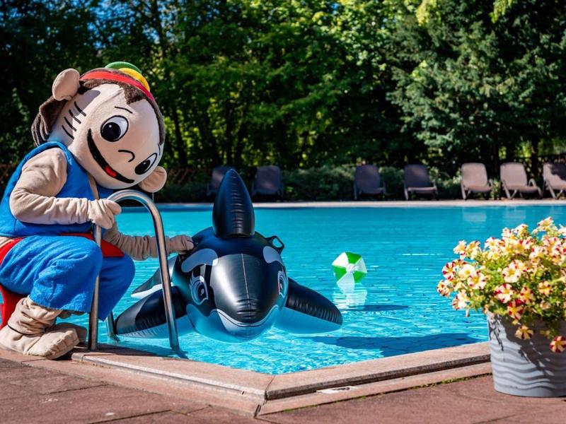 Persoon in groot mascottekostuum knielt aan het zwembad naast een opblaasbare orka.