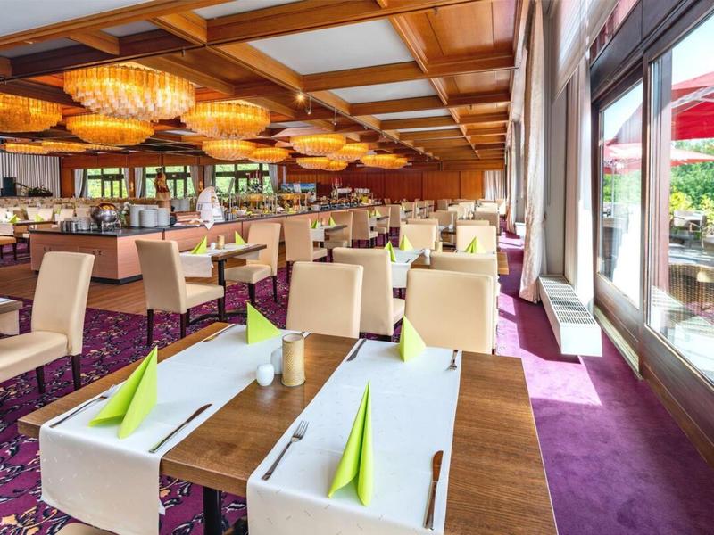 Licht restaurant met grote ramen, moderne stoelen en decoratieve plafondlampen.