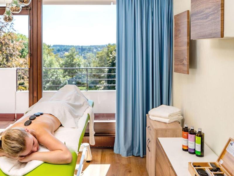 Lichte massageruimte met uitzicht op groene omgeving en blauwe gordijn.