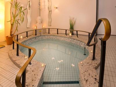 Innen-Whirlpool mit Treppe, Handläufen und Kerzen auf Mosaikfliesen in warm beleuchtetem Raum.