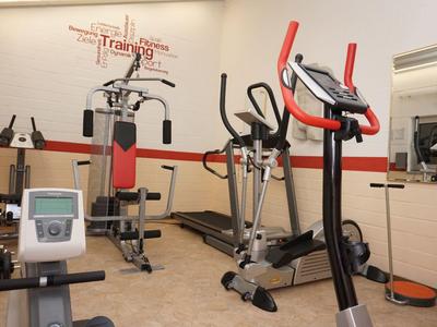 Kleiner Fitnessraum mit verschiedenen Trainingsgeräten und Spiegel an der Wand.