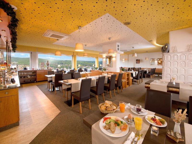 Moderner, heller Restaurantraum mit gedeckten Tischen, gelber Decke und Holz- sowie Lederstühlen.