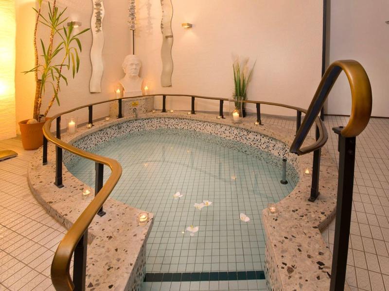 Innen-Whirlpool mit Treppe, Handläufen und Kerzen auf Mosaikfliesen in warm beleuchtetem Raum.