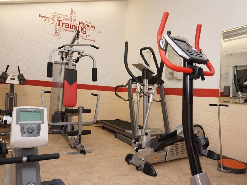 Kleiner Fitnessraum mit verschiedenen Trainingsgeräten und Wandspiegel.