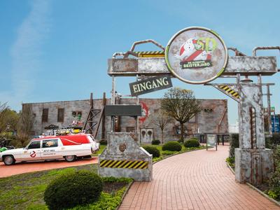 Eingang zu einem Themenpark mit Ghostbusters-Autos und nostalgischem Tor unter blauem Himmel