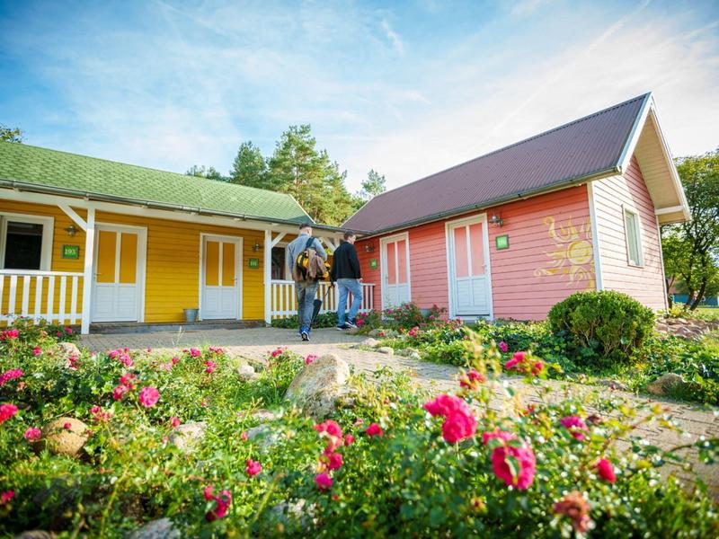 Para stoi przed dwoma kolorowymi domkami letniskowymi z ogrodem i kwiatami pod niebieskim niebem.