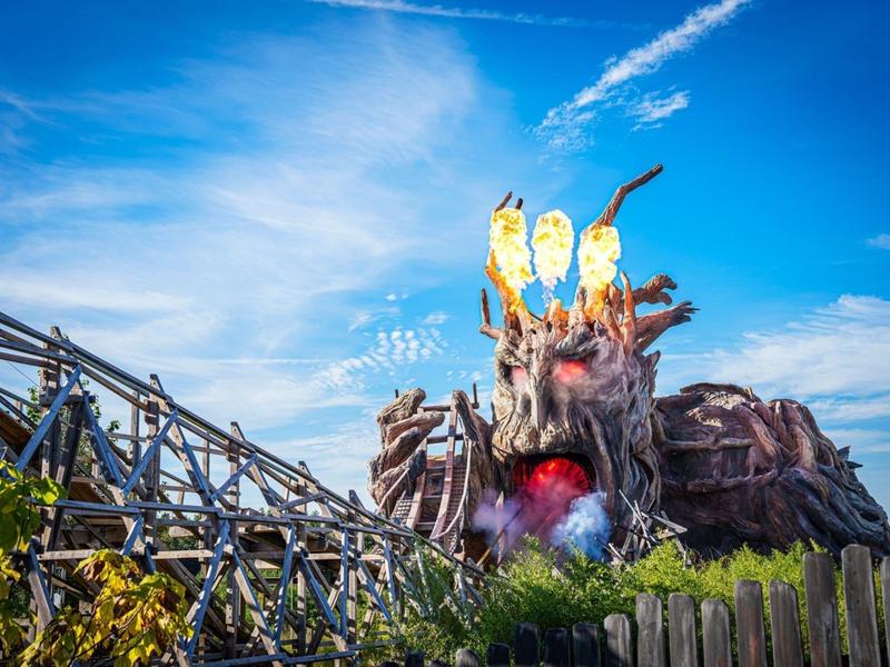 Kolorowy drewniany rollercoaster z głową smoka i niebieskim niebem w parku rozrywki