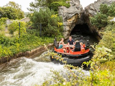 Menschen fahren in einem Geländeboot auf einem Wasserfluss, der in eine künstliche Höhle führt.