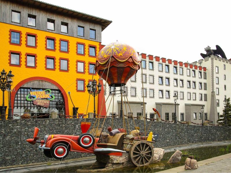 Kolorowa atrakcja przejażdżki balonem na tle pomarańczowo-białego budynku z wieloma oknami.