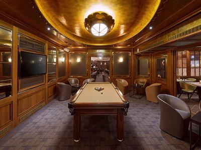 Eleganter Spielraum mit Billardtisch, Holzpaneelen, warmem Licht und bequemen Sesseln in dunklem Ton.