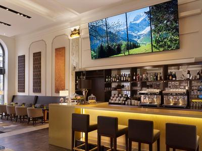 Moderner Hotelbarbereich mit gemütlichen Sitzgelegenheiten und Berglandschaft an Wandbildschirm.