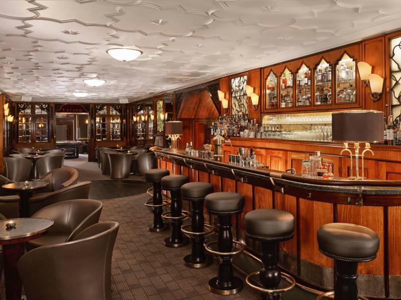 Gemütliche Bar mit Holztheke, Lederhockern und braunen Ledersesseln in warmem Licht.