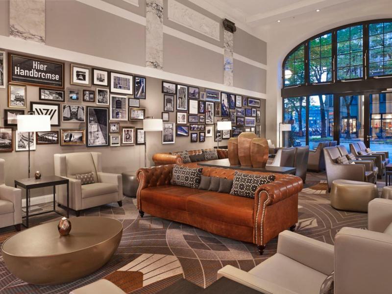 Gemütlicher Lounge-Bereich mit braunen Ledersofas, hellen Sesseln, vielen Bildern und großem Fenster.