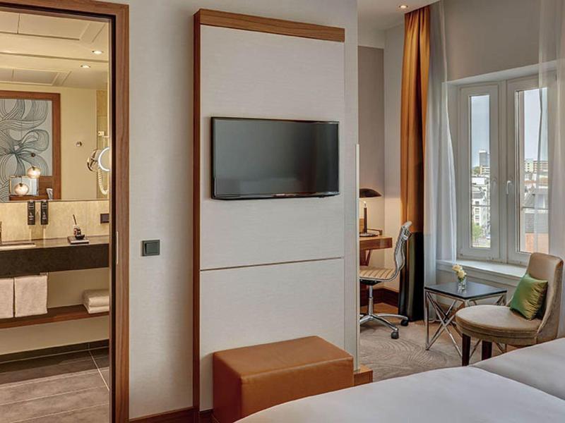 Modernes Hotelzimmer mit Fernseher, Schreibtisch, Stuhl und angrenzendem Badezimmer.