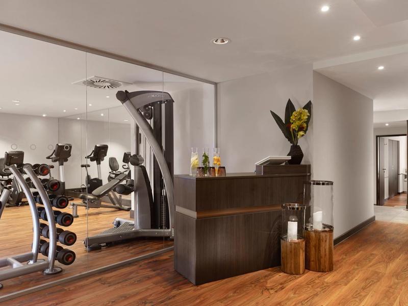 Moderner Fitnessraum mit Hanteln, Trainingsgeräten und einer dunklen Theke vor hellen Wänden.