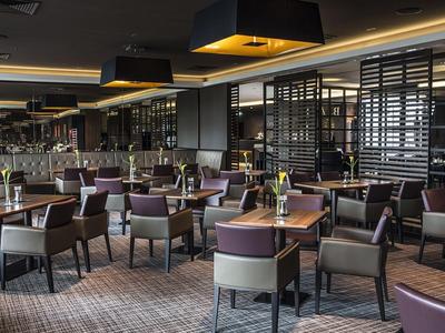 Elegantes Restaurant mit gedeckten Tischen und modernen Stühlen in warmem Licht.