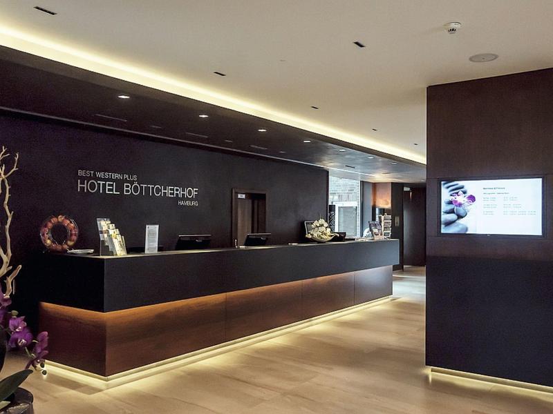 Moderne Hotelrezeption mit schwarzem Tresen, heller Holzfußboden und indirekter Beleuchtung.