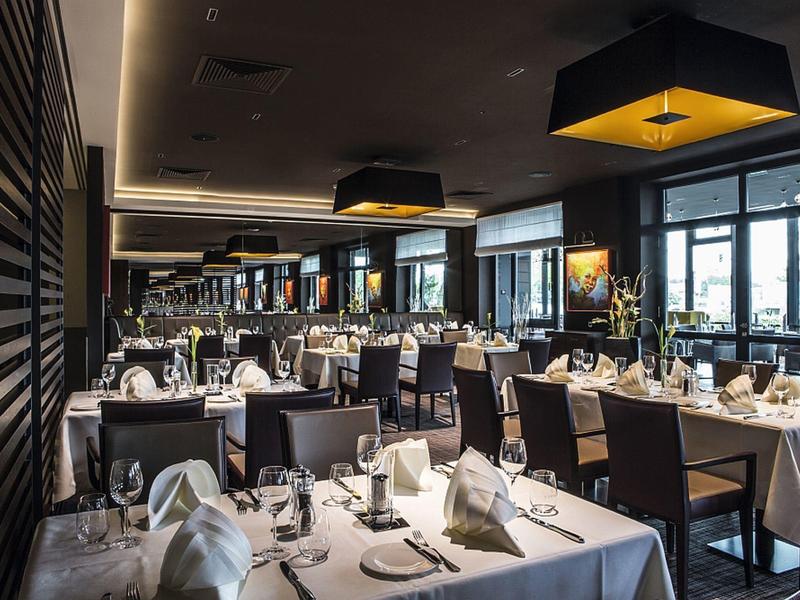 Modernes Restaurant mit elegant gedeckten Tischen, schwarzen Stühlen und großem Fensterfront.